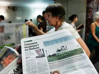 An employee distributes newspapers, with a photograph (L) of former U.S. spy agency contractor Edward Snowden seen on a page, at an underground walkway in central Moscow