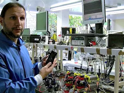 Dr Ioannis Ieropoulos in his laboratory at the Bristol Robotics Laboratory holding a phone powered by a microbial fuel cell stack