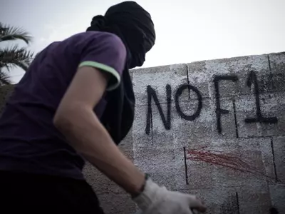 A Bahraini masked protestor writes graffiti against the upcoming Bahrain Formula One Grand Prix.