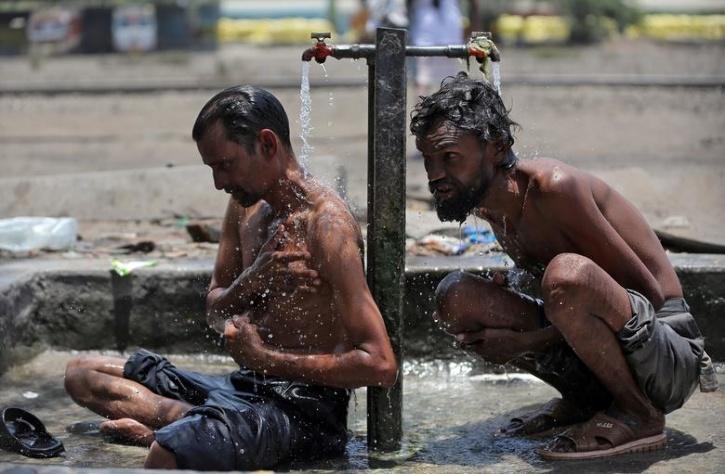 Men bathe at municipal taps along railway tracks, at a yard, on a hot day in Ahmedabad, India,