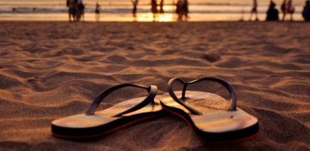 capture-of-flip-flops-in-sand-at-sunset-with-beachgoers-along-the-shore-in-the-background-6267cf12d3fca