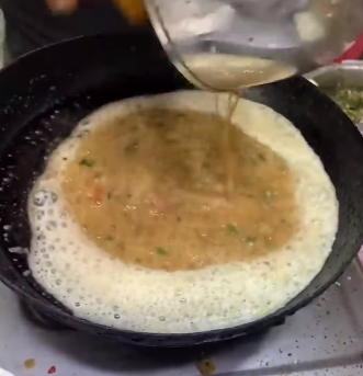 A street food vendor prepares an omelet with crackers and Parle-G cheese