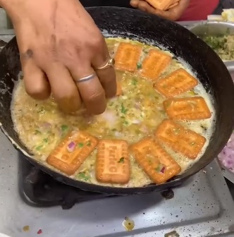 A street food vendor prepares an omelet with crackers and Parle-G cheese