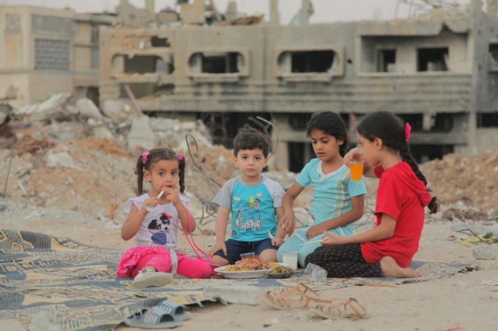 Children Eating in front of the rubble of their homes