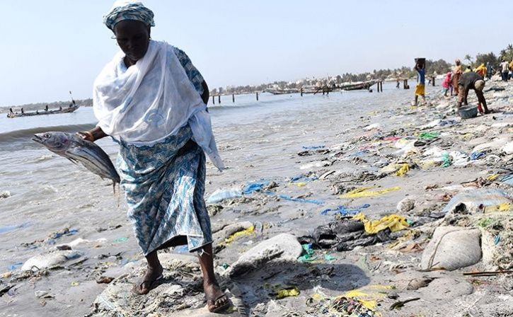 A woman holding a fish walks on tyre and plastic waste on June 1, 2019 in Dakar