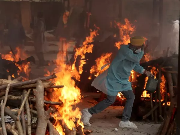 A volunteer runs to avoid heat emitting from the burning funeral pyres of COVID-19 victims at a crematorium in Jammu.